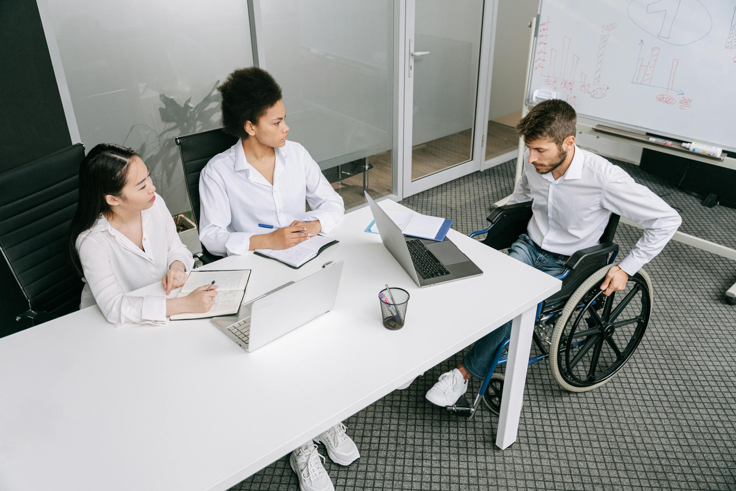 A diverse group of colleagues in a business meeting discussing ideas indoors, one of them is an example of employees with a disability