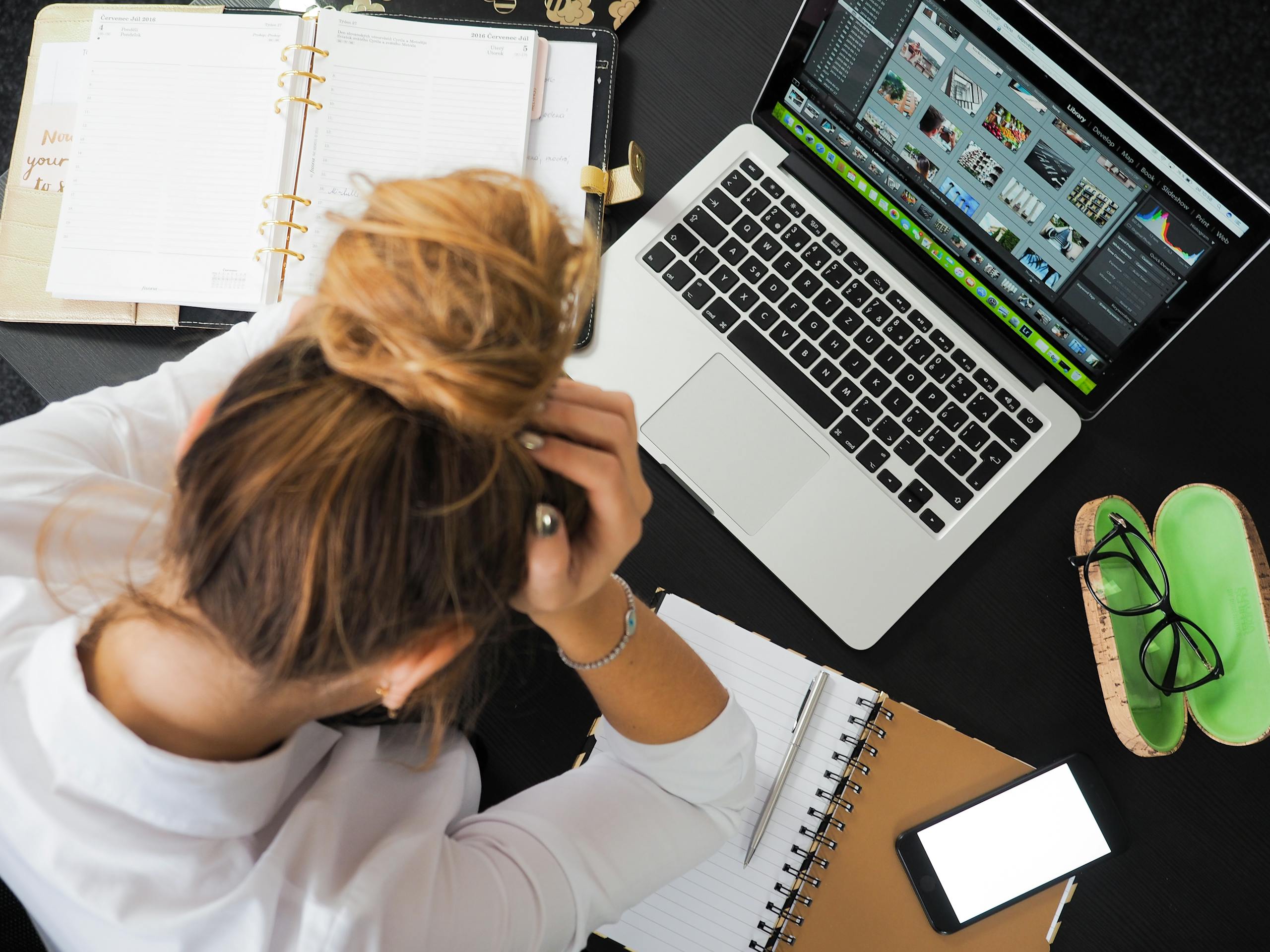 Overhead view of a stressed woman sitting at a desk with a laptop, phone, and notebooks, possibly symbolising a resignation through conclusive conduct